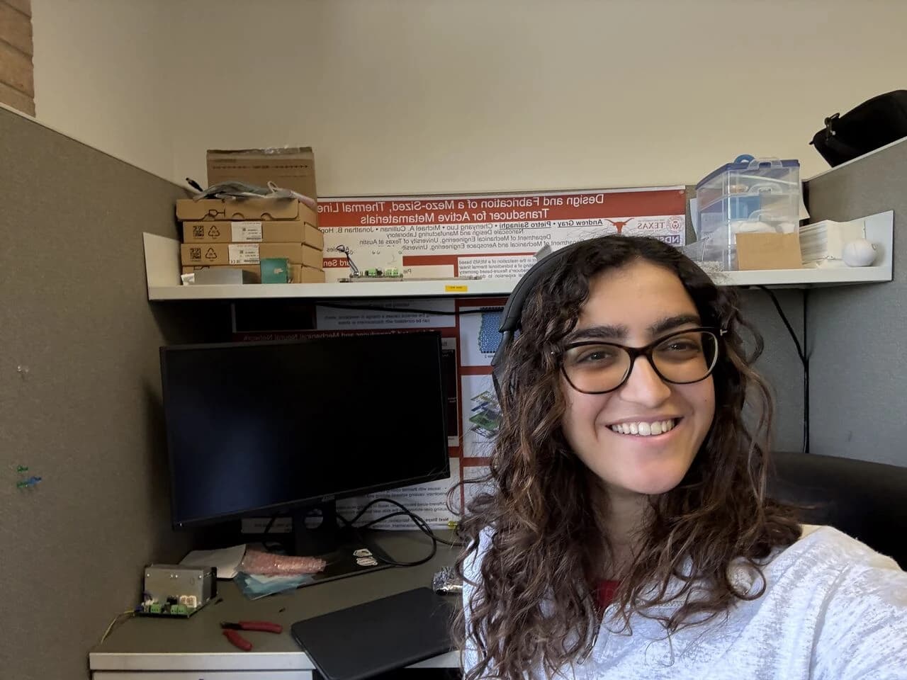 Aita at her desk in the Nanoscale Design and Manufacturing Laboratory, a lab research poster on the shelf behind her